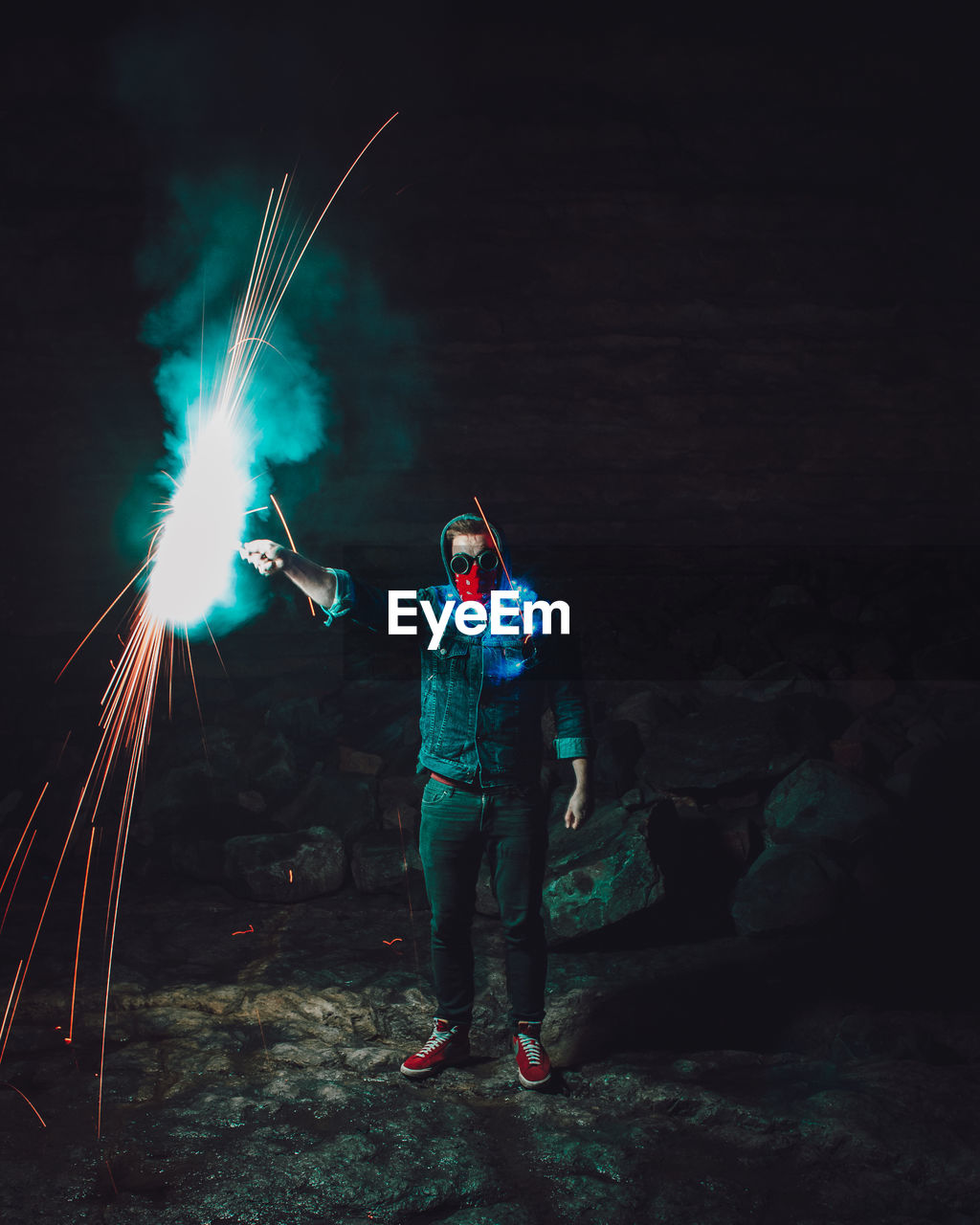 Man with firework standing on rock at night