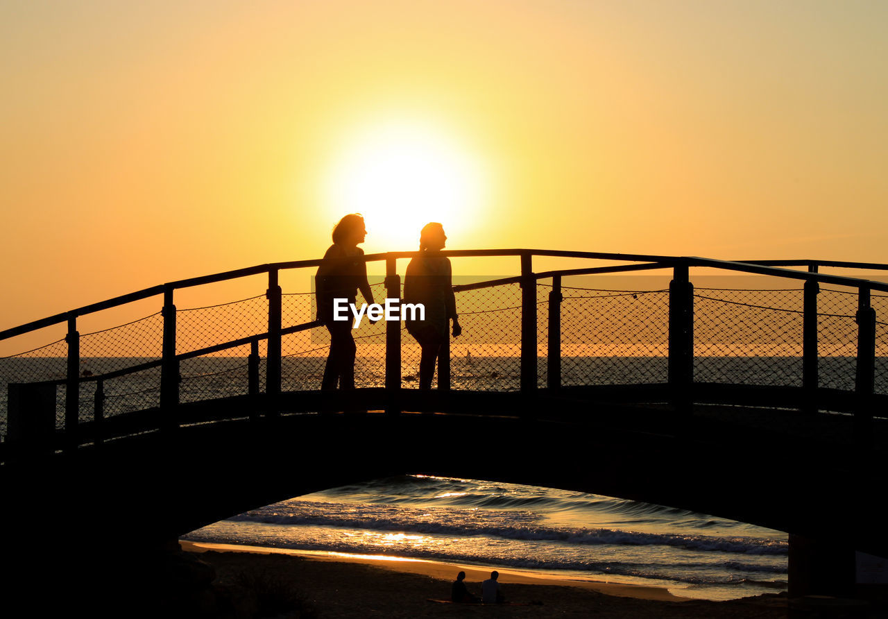 SILHOUETTE PEOPLE ON RAILING AGAINST SEA