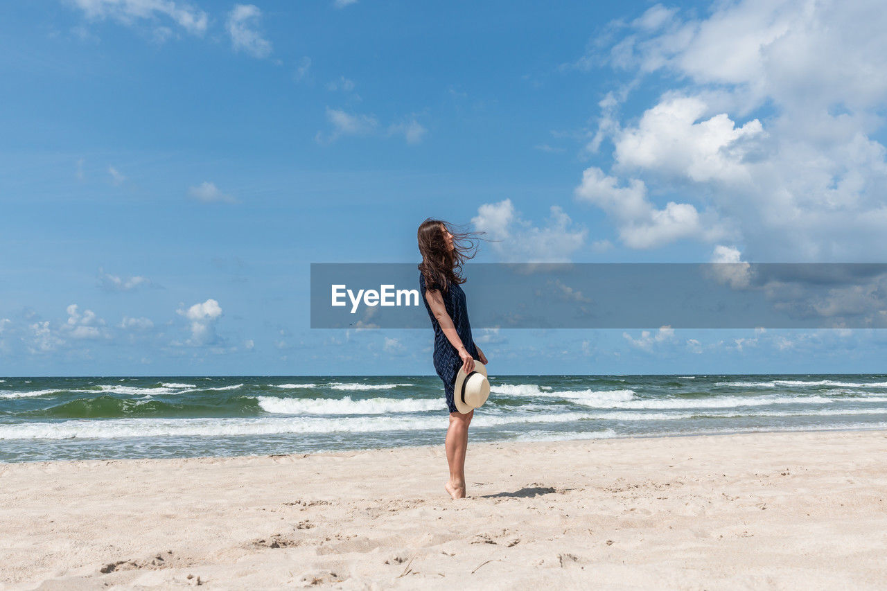 rear view of young woman standing at beach against sky