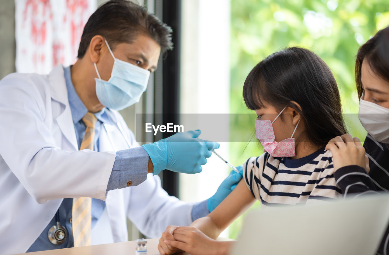 Doctor wearing mask vaccinating girl at clinic