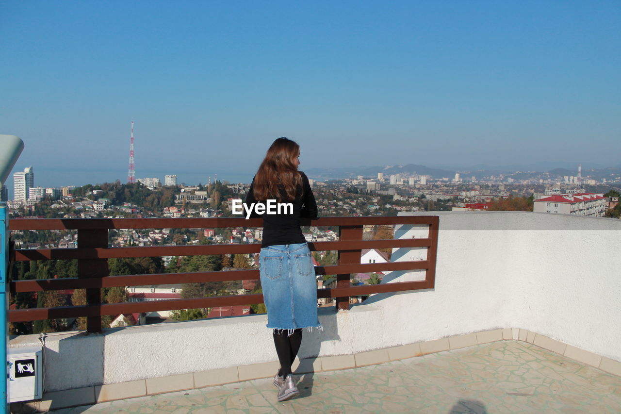 Rear view of woman looking at cityscape against clear sky