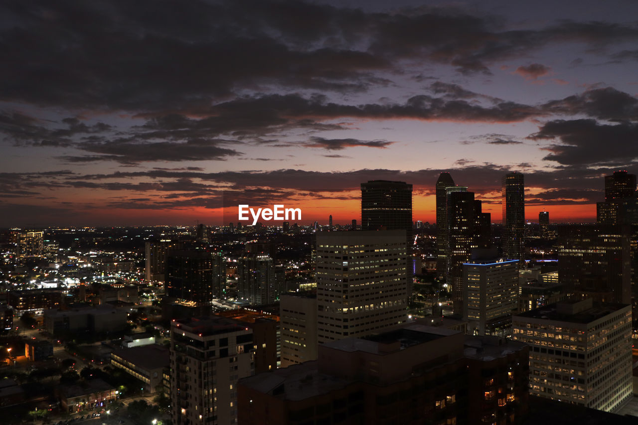 HIGH ANGLE VIEW OF ILLUMINATED BUILDINGS IN CITY AGAINST SKY DURING SUNSET