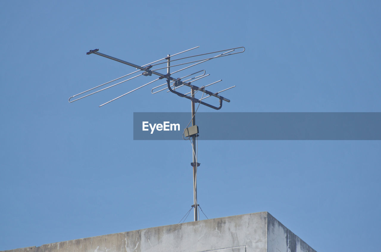 television antenna, wind, sky, architecture, clear sky, built structure, day, blue, nature, communication, mast, no people, antenna, low angle view, technology, sunny, outdoors, electricity, roof, television aerial, renewable energy, weather vane, copy space, overhead power line, line, building exterior, telecommunications equipment