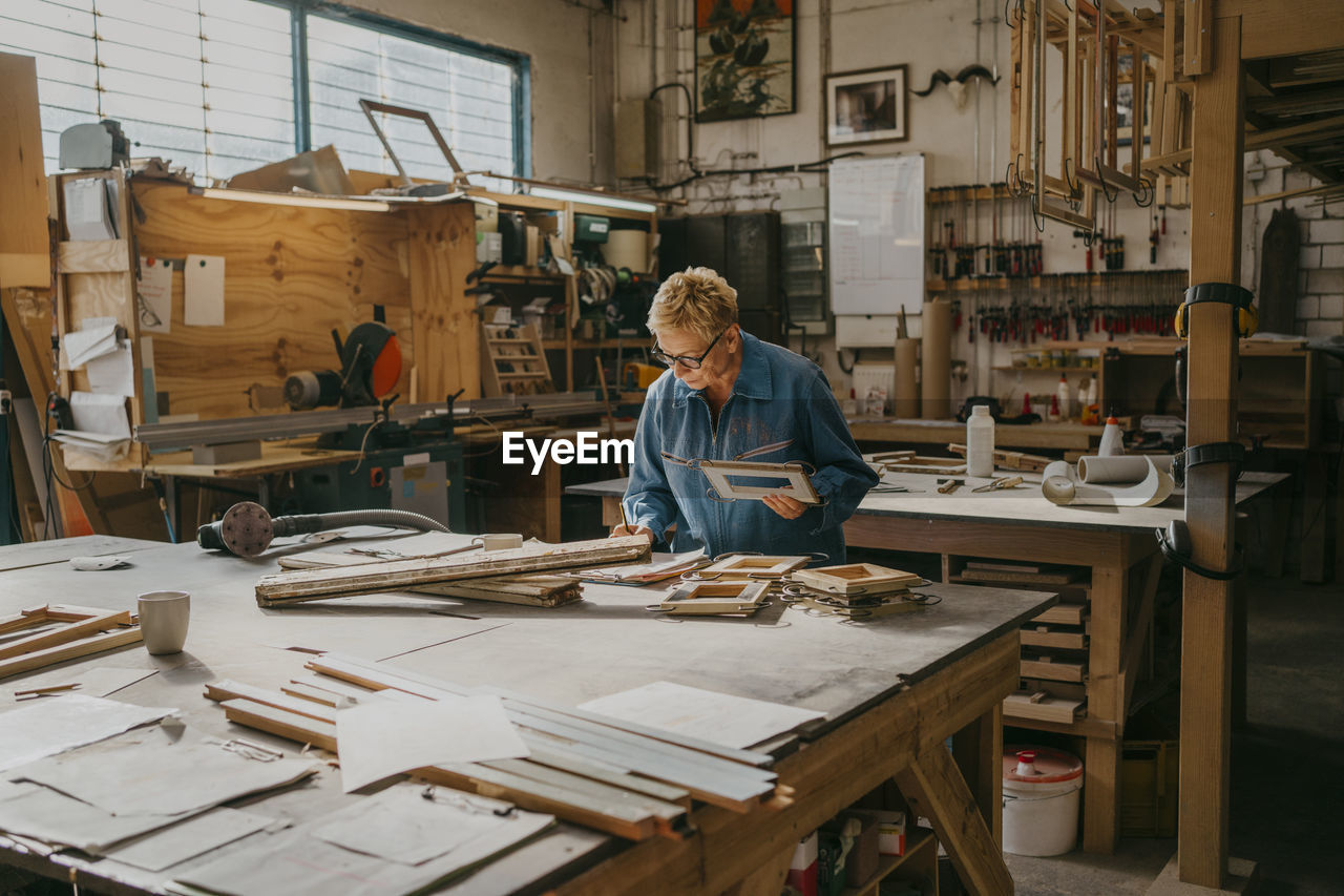 Senior female carpenter holding frame while working at workshop