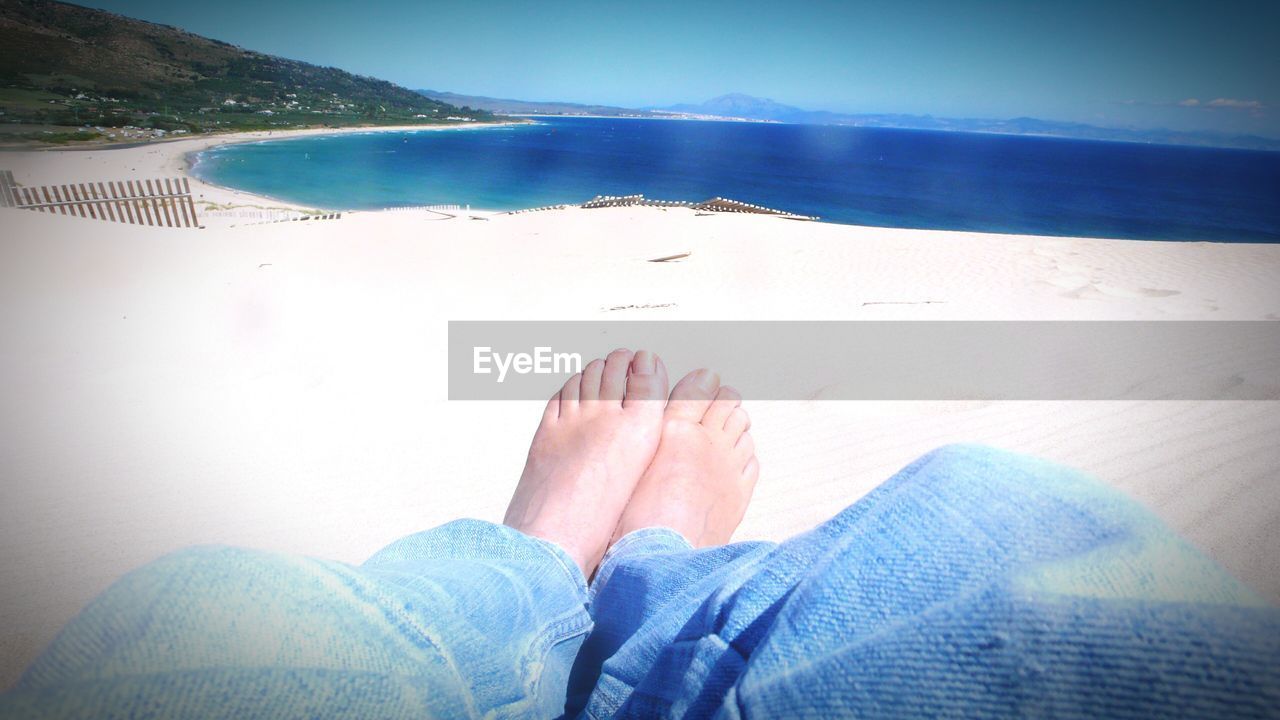 LOW SECTION OF WOMAN RELAXING ON SANDY BEACH