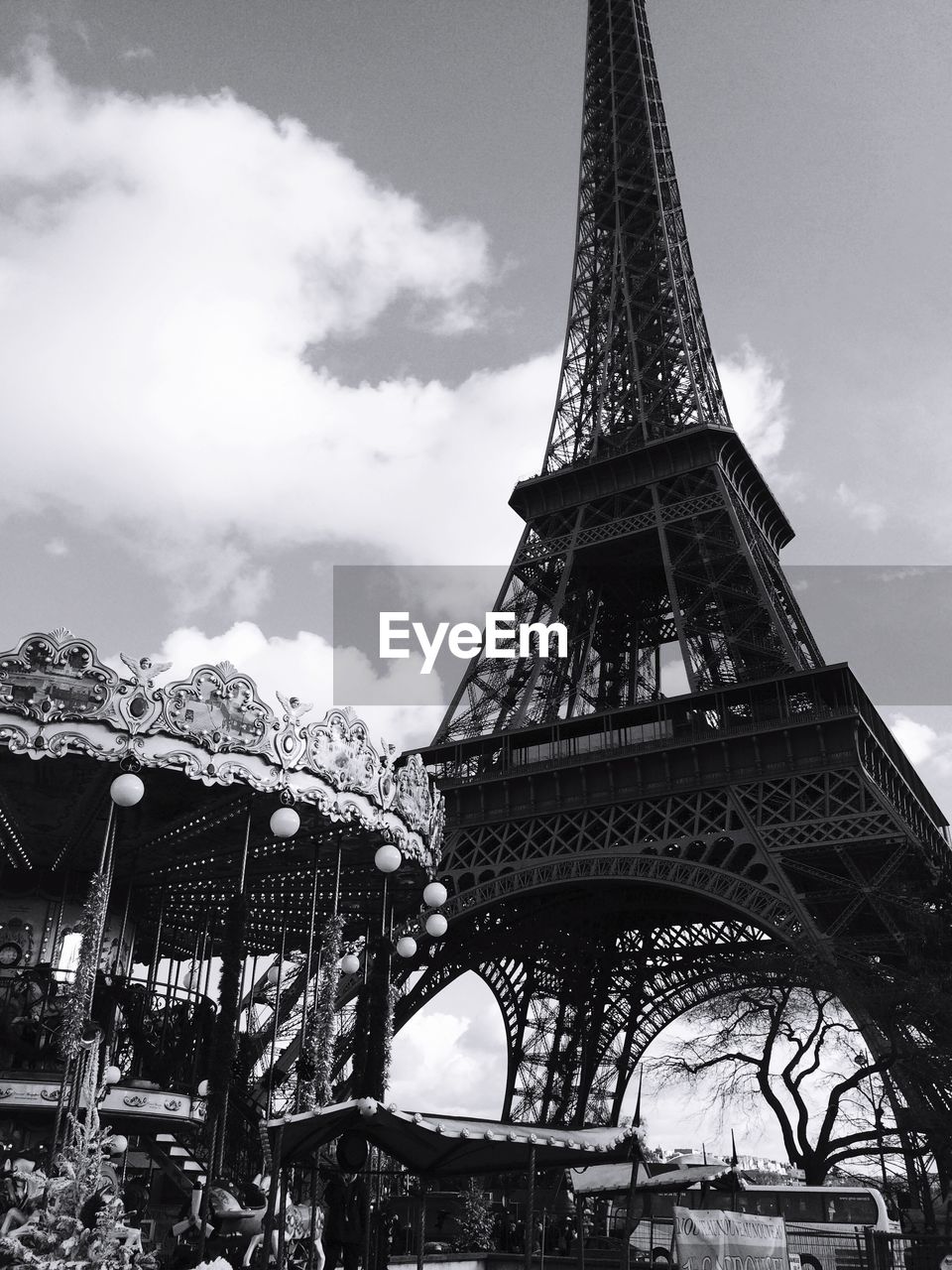 Low angle view of eiffel tower and carousel against cloudy sky in city