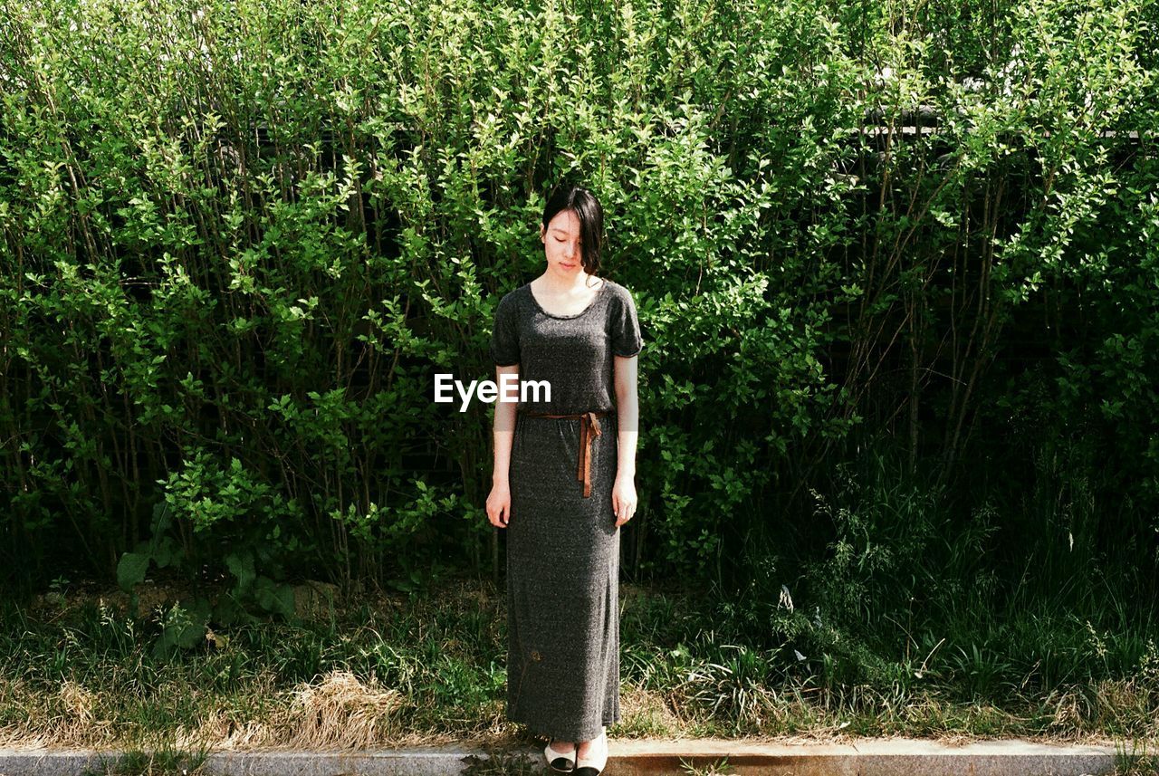 Full length of sad young woman standing against plants