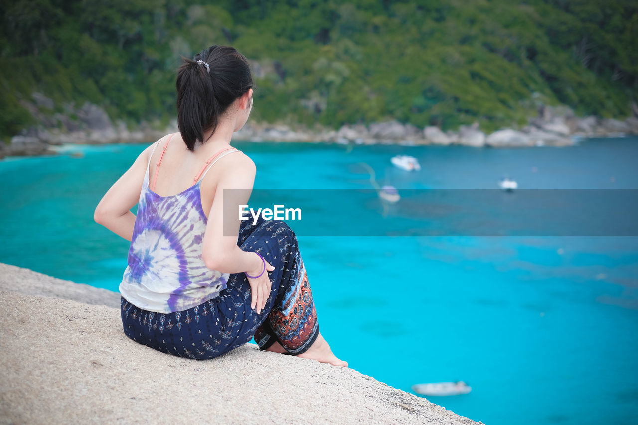 Rear view of woman sitting by sea 