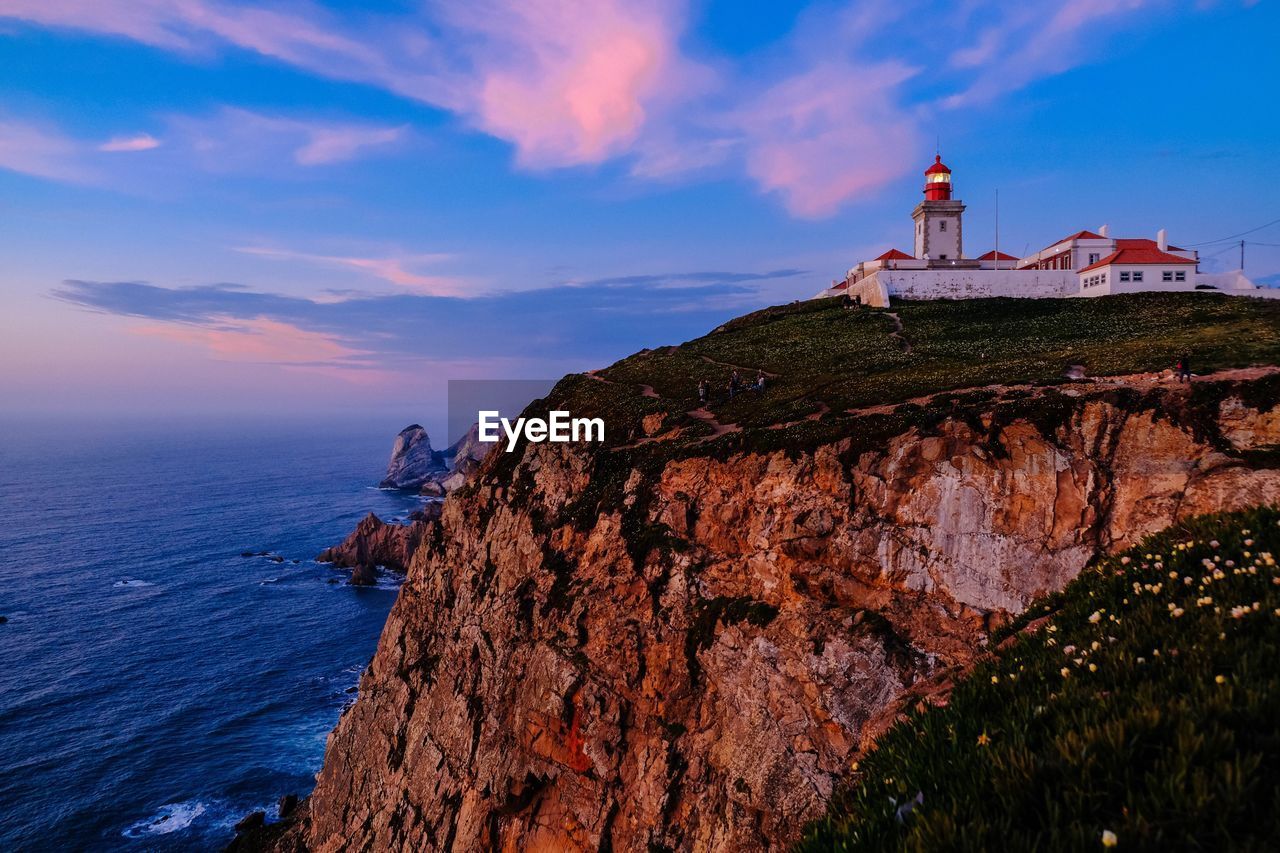 Lighthouse by sea against sky during sunset