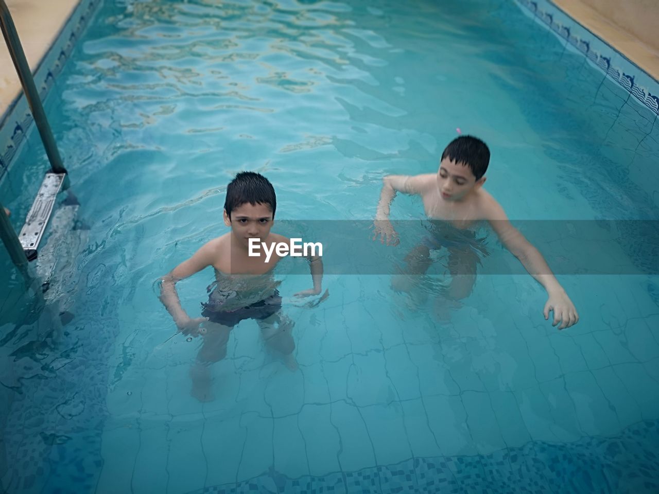 HIGH ANGLE VIEW OF SHIRTLESS BOY SWIMMING IN POOL
