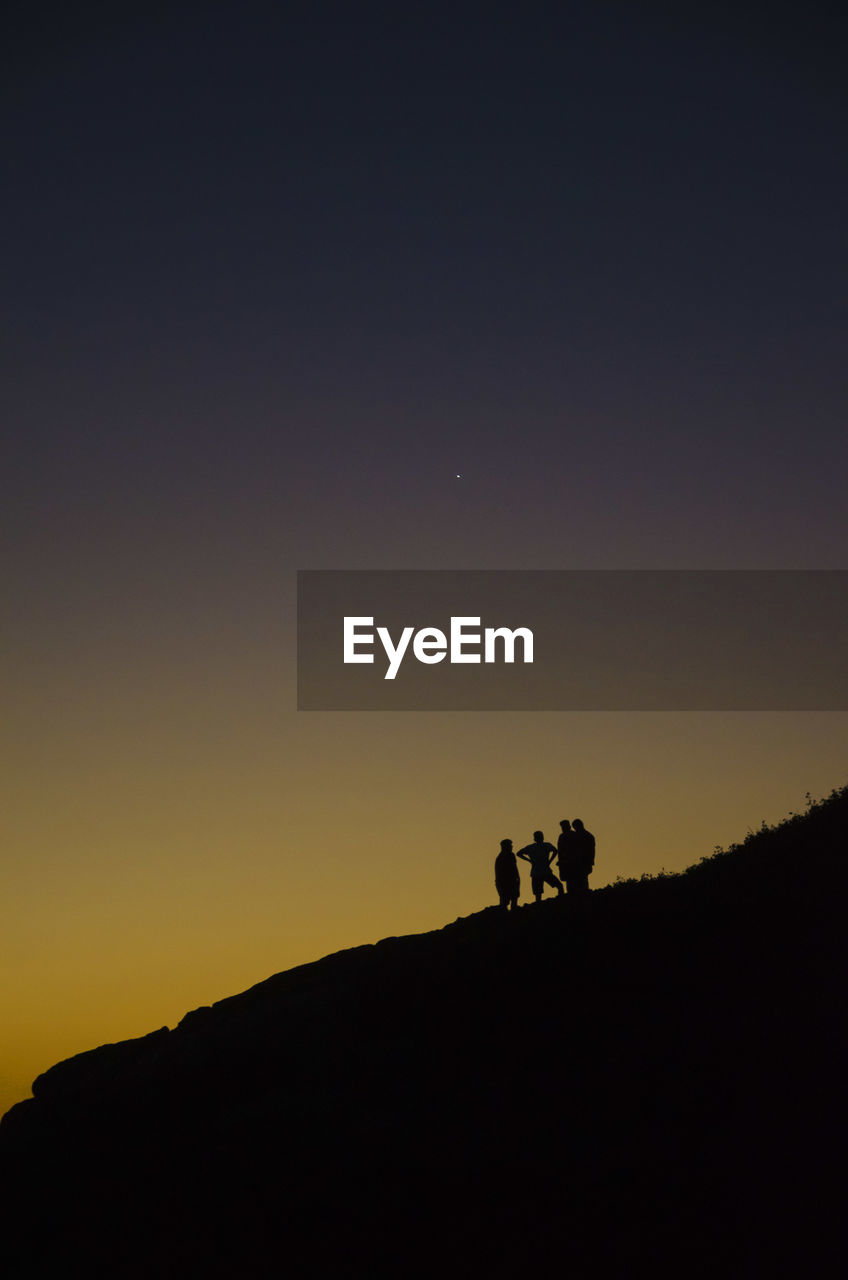 Low angle view silhouette of people standing on mountain against sky during sunset