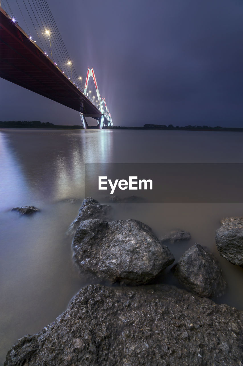 Illuminated bridge over sea against sky at night