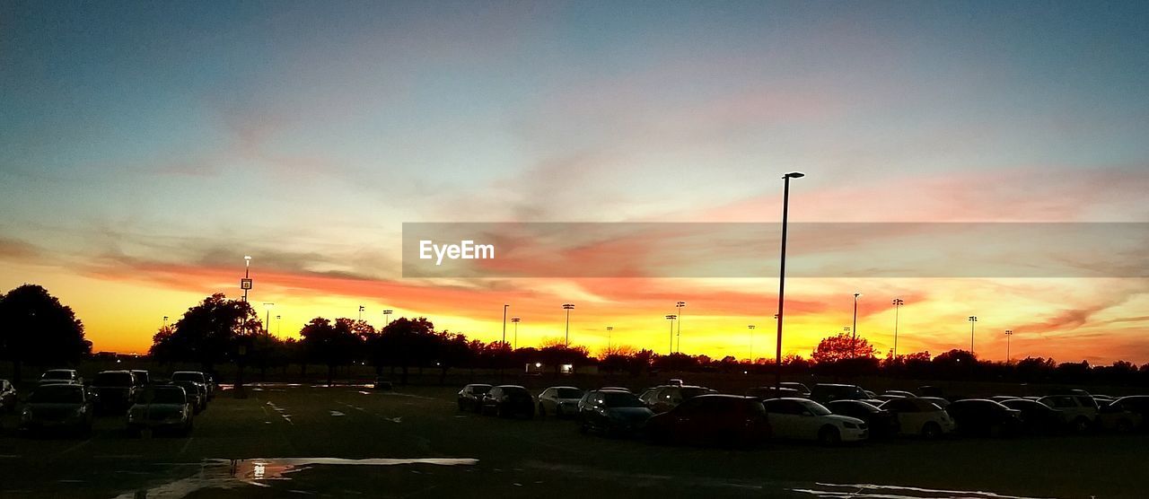 Panoramic view of vehicles in parking lot against sky during sunset
