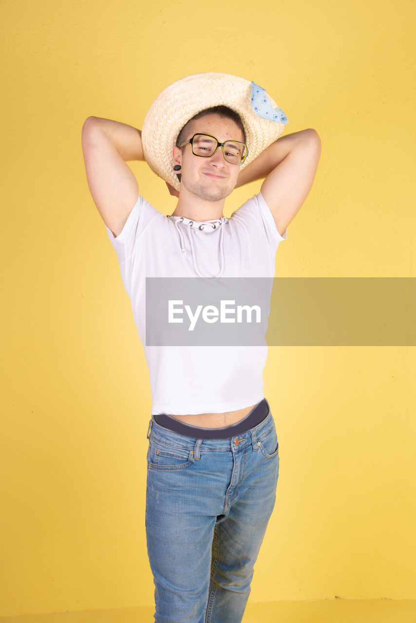 Portrait of smiling young man wearing hat standing against yellow background