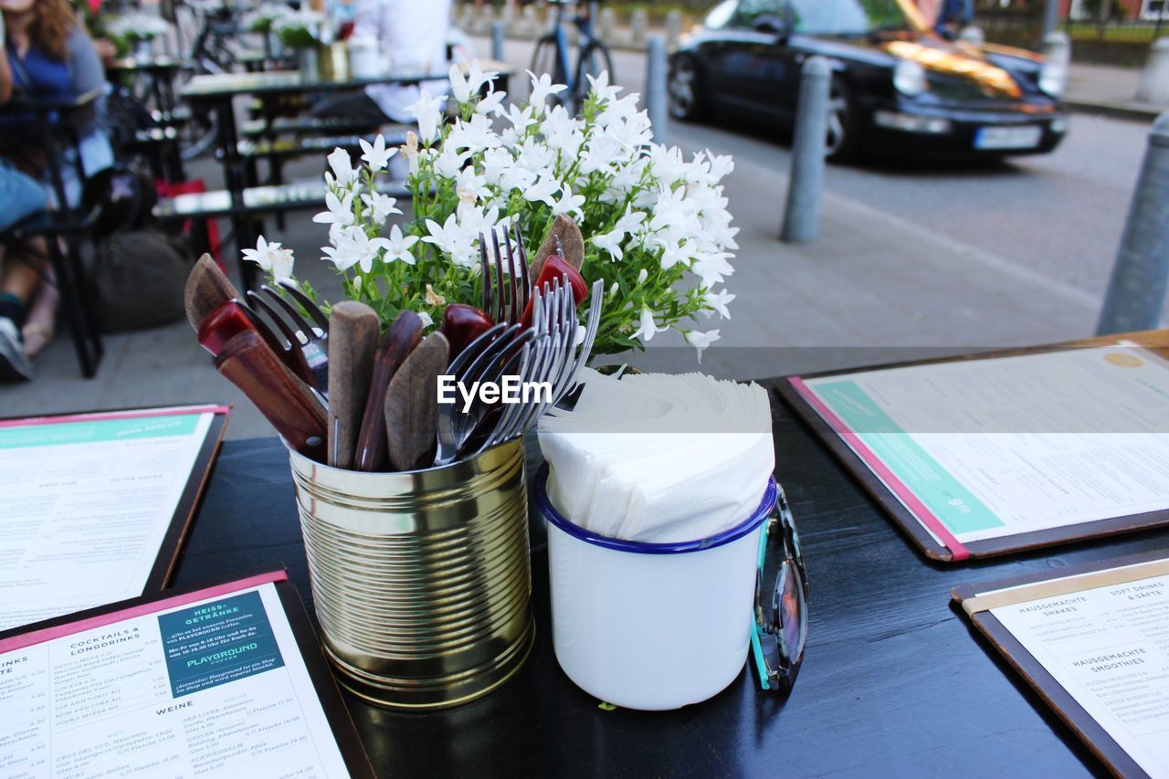 Close-up of cutlery in container by flowers at sidewalk cafe