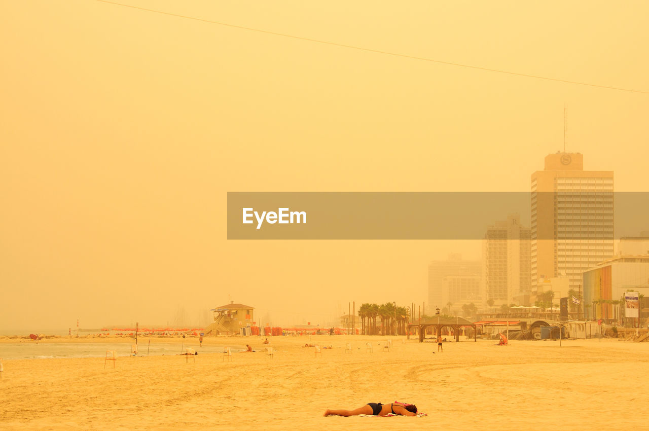 Woman in bikini relaxing at beach against sky in city