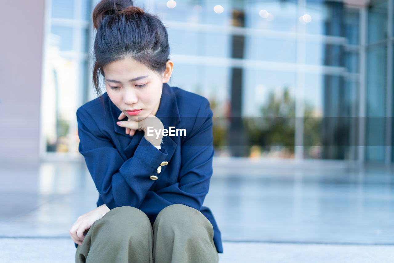 Depressed young woman sitting outdoors against building