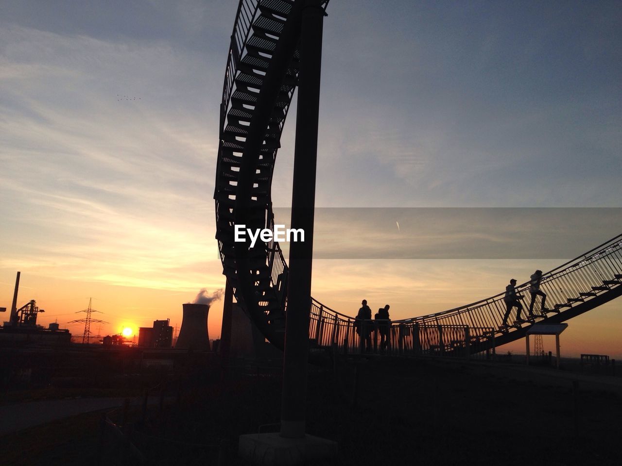 Silhouette people walking on tiger and turtle magic mountain against orange sky