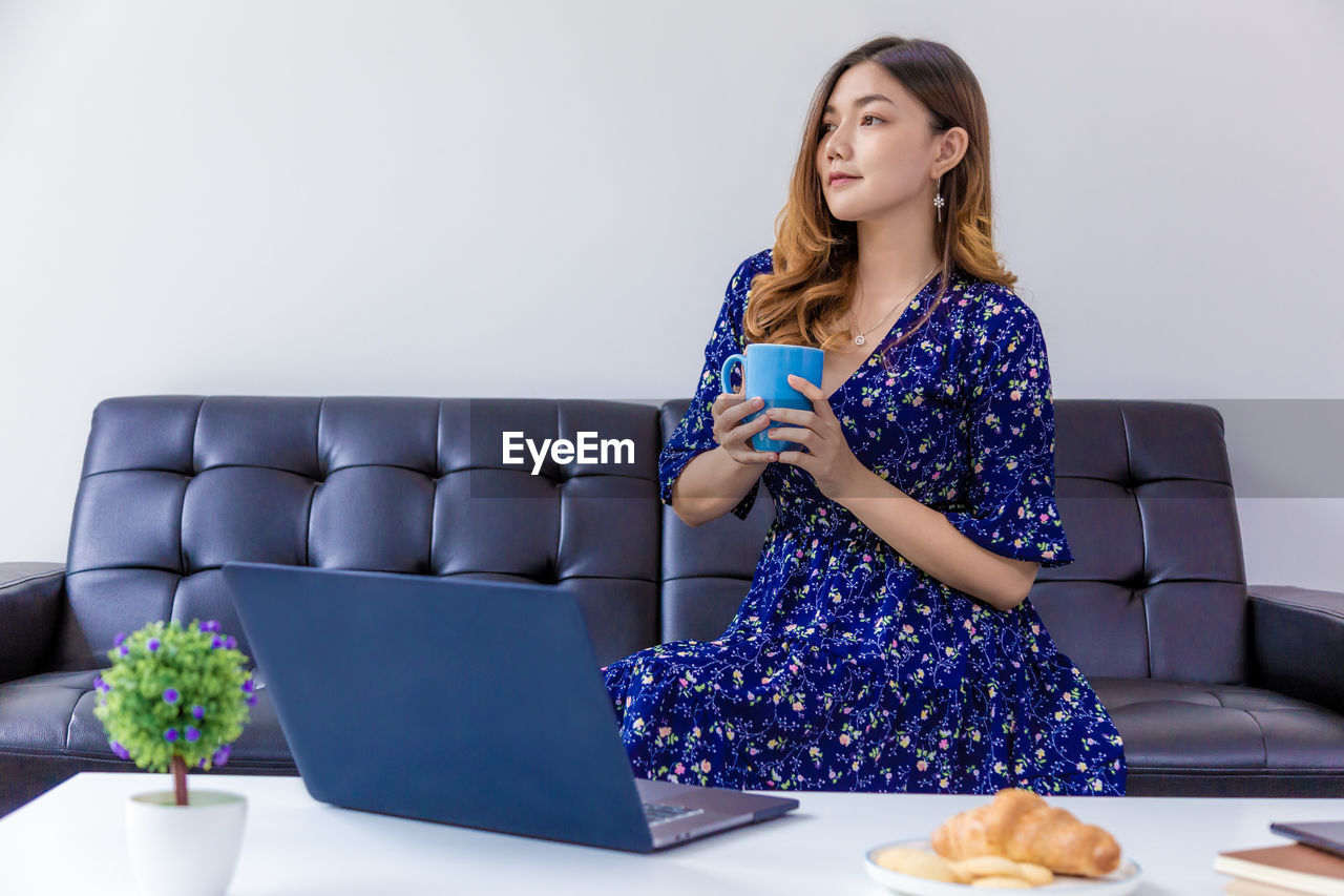 YOUNG WOMAN LOOKING AWAY WHILE SITTING ON LAPTOP