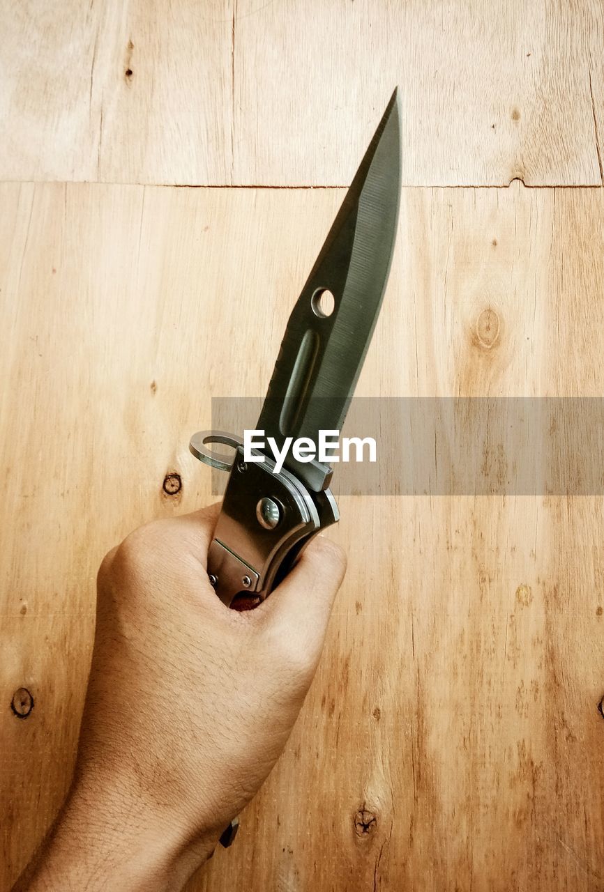 Close-up of hand holding knife on wooden table