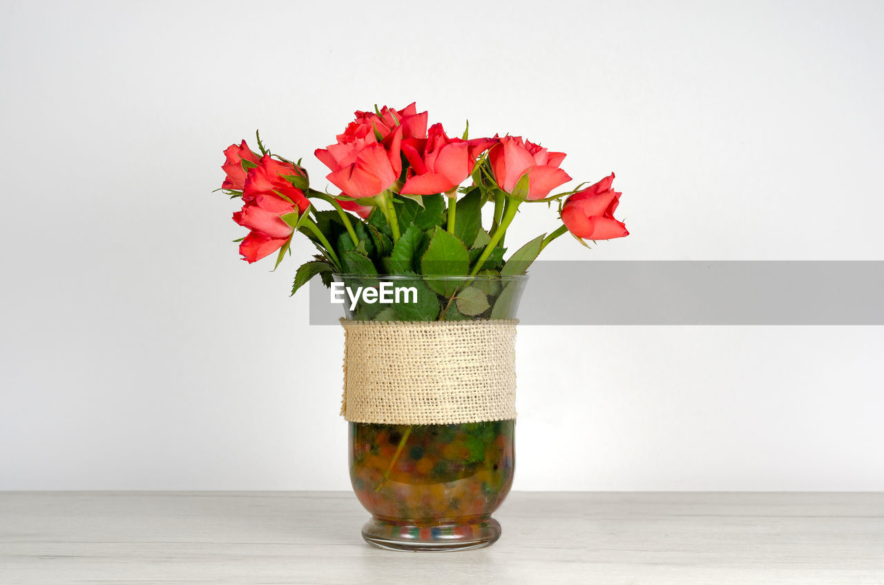 CLOSE-UP OF RED FLOWER VASE ON TABLE AGAINST WALL