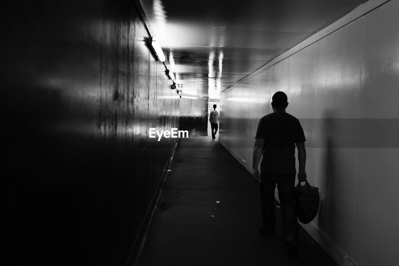 Rear view of silhouette man walking in illuminated tunnel