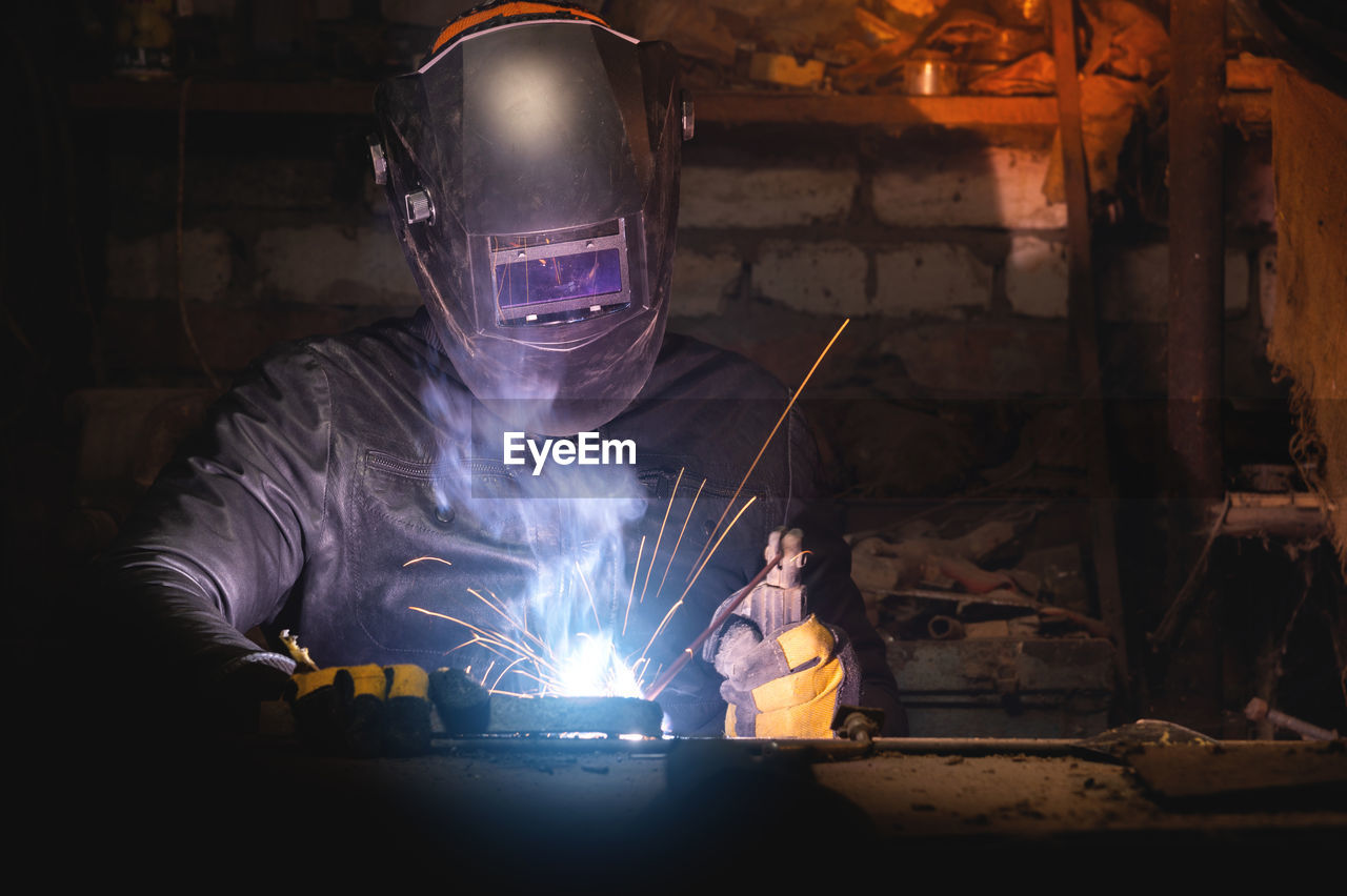 Village workshop, welding in an old garage. an unrecognizable man repairs a metal part wearing