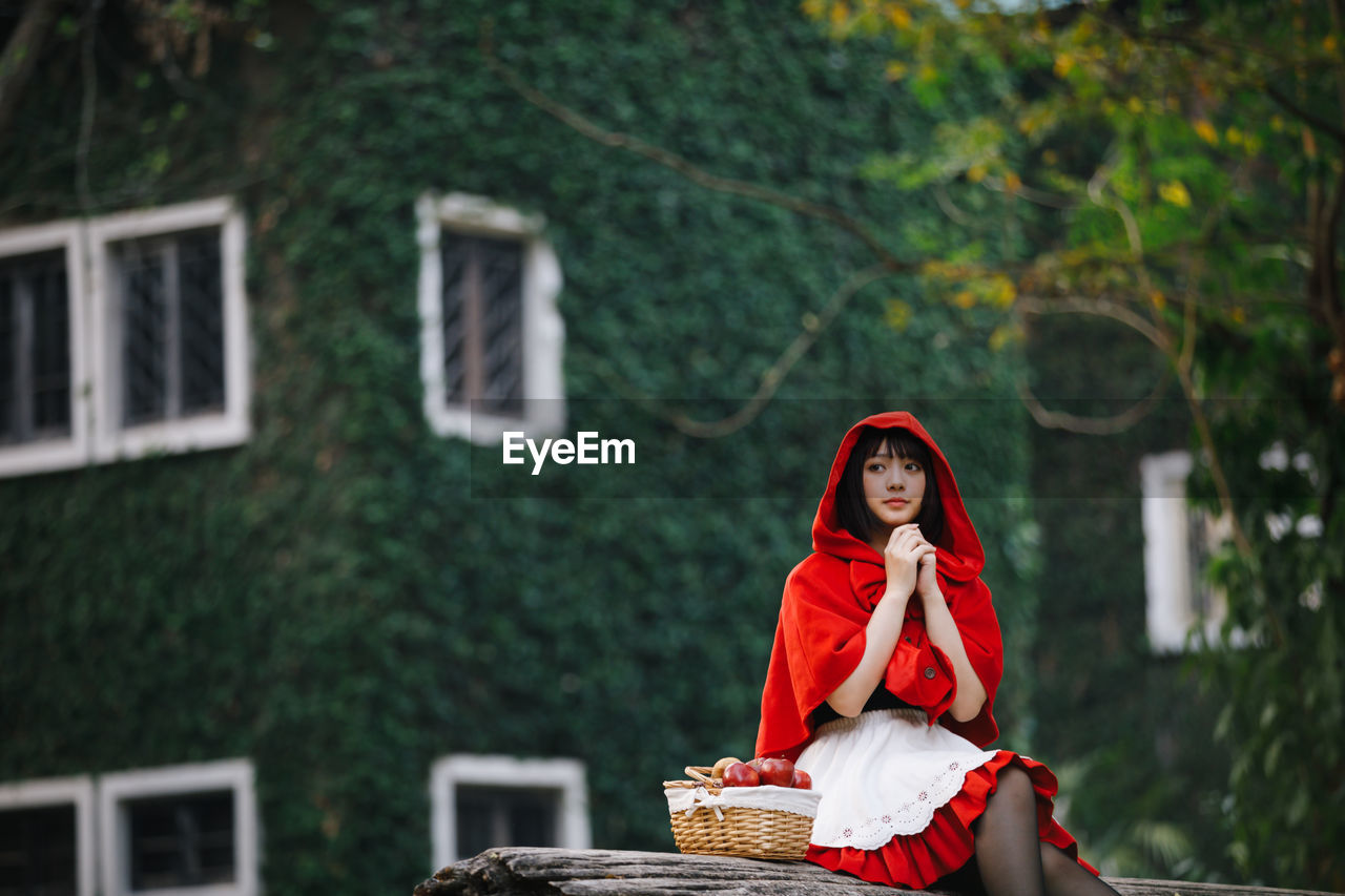 Young woman with fruits in basket looking away while sitting against house