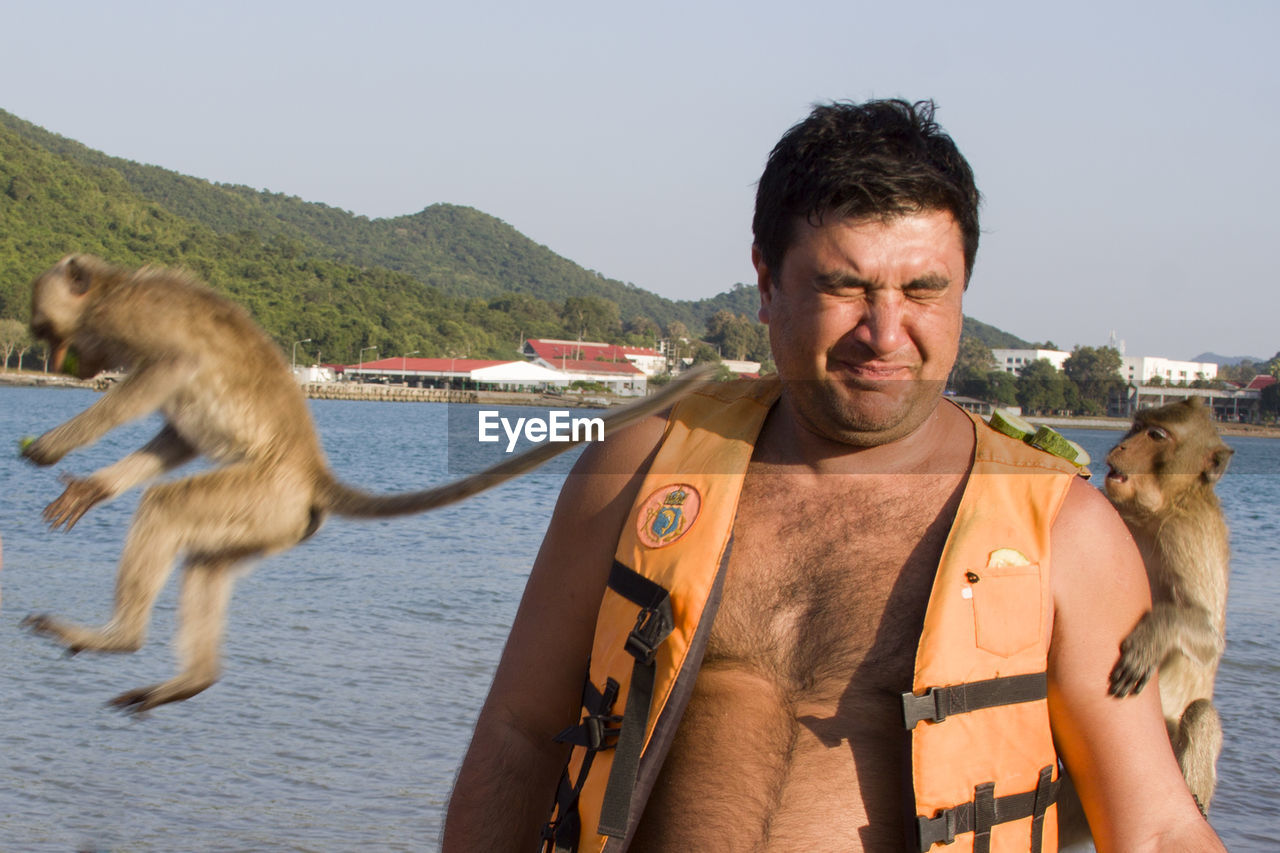 Man wearing life jacket amidst monkeys at beach