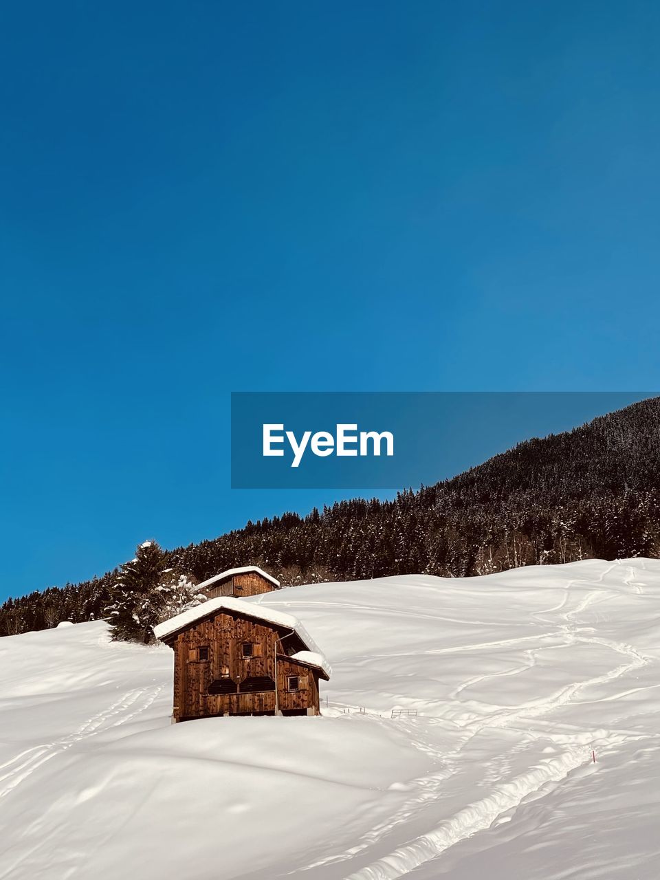 Traditional built structure on snow covered alpine land against clear blue sky