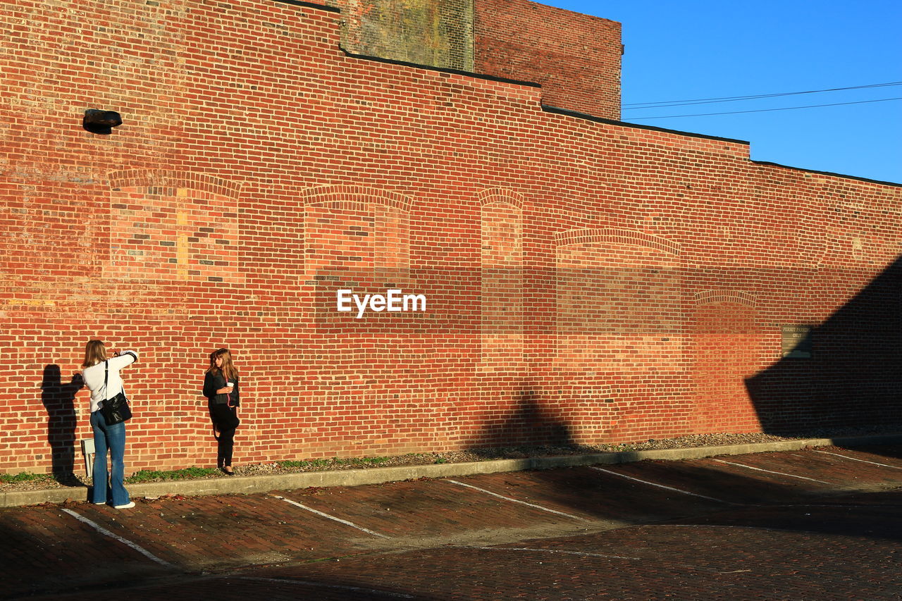 Wide angle of two girls taking pictures against brick wall