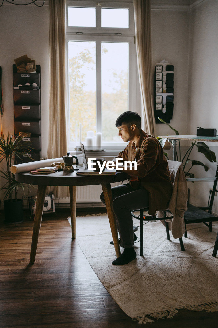 Young male freelancer working on laptop while sitting at home office