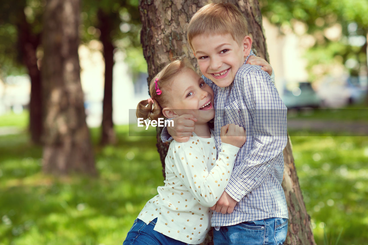 Portrait of smiling sibling embracing while standing at park