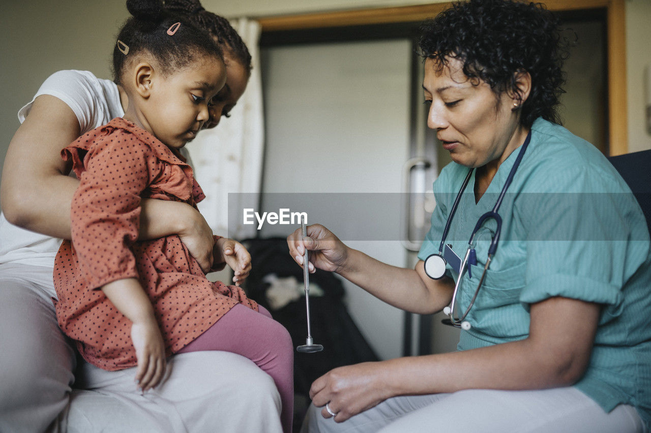 Female doctor with reflex hammer examining girl in clinic