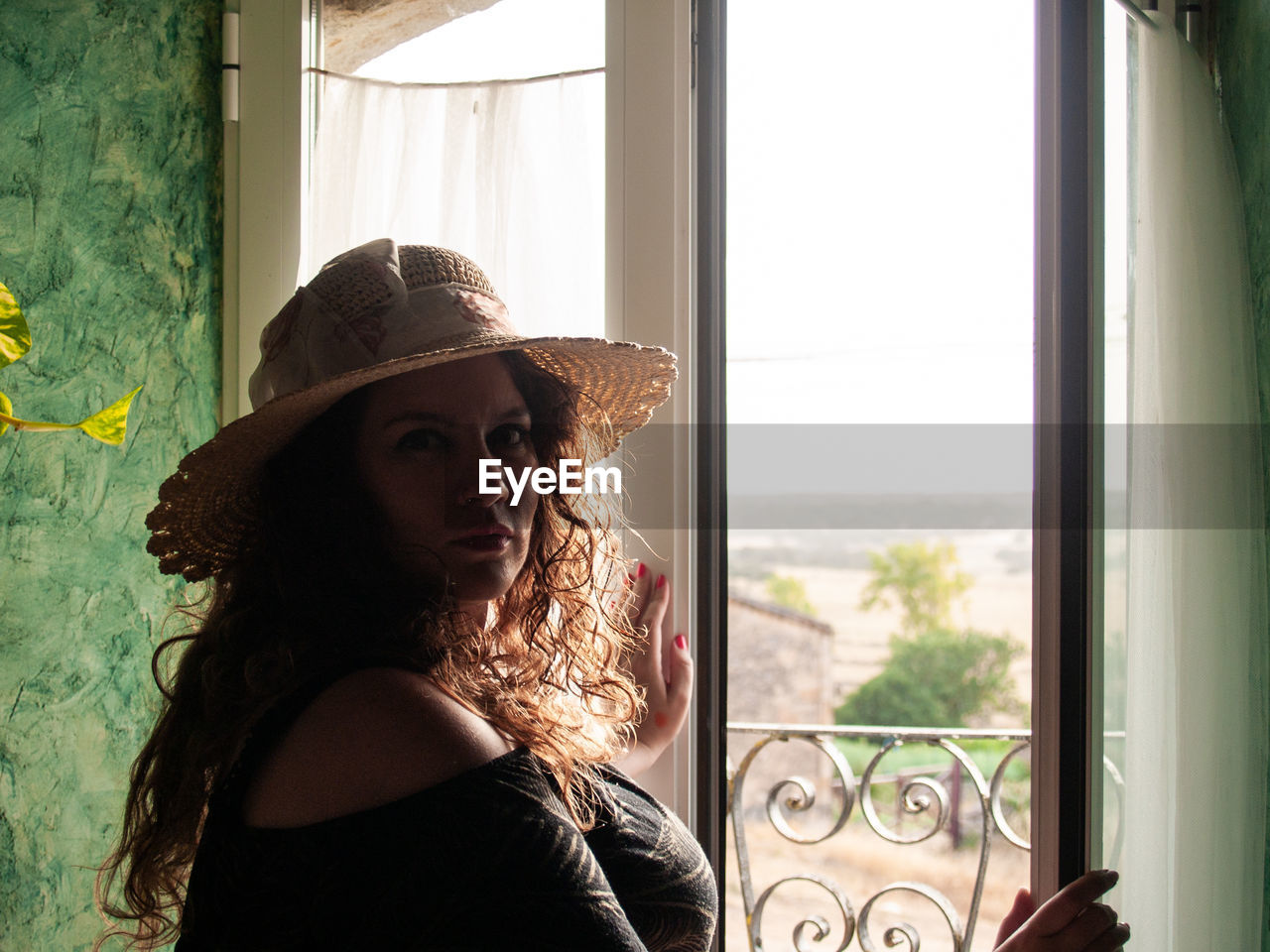 Portrait of woman wearing hat while standing against window at home