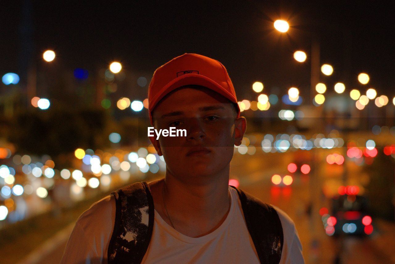 Portrait of young man standing against illuminated city at night