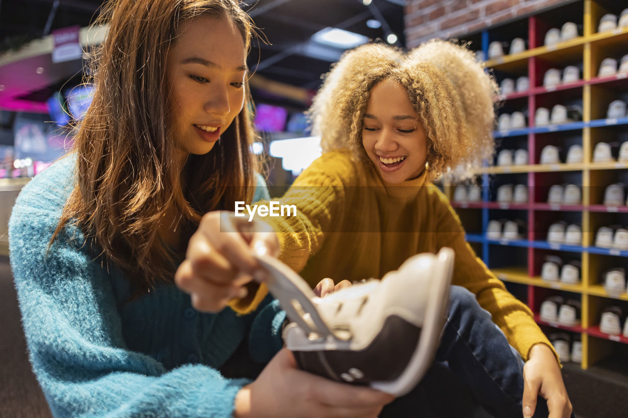 Happy woman with friend looking at bowling shoes