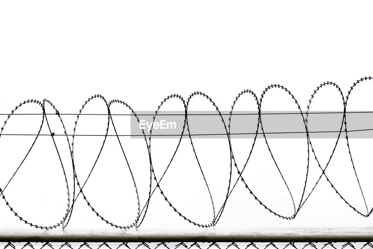 Close-up of barbed wire fence against white background