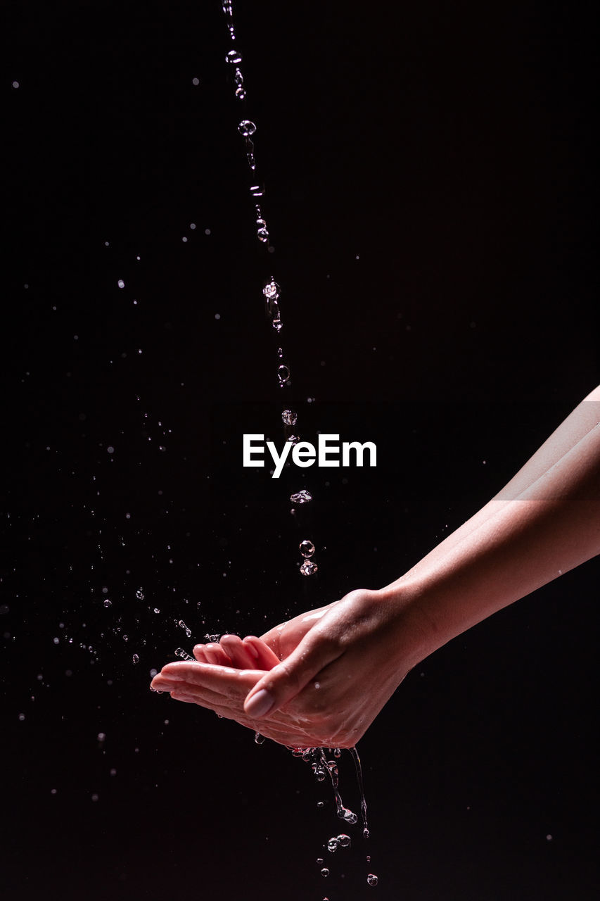 Crop view of anonymous woman washing hands with splashing water against black background