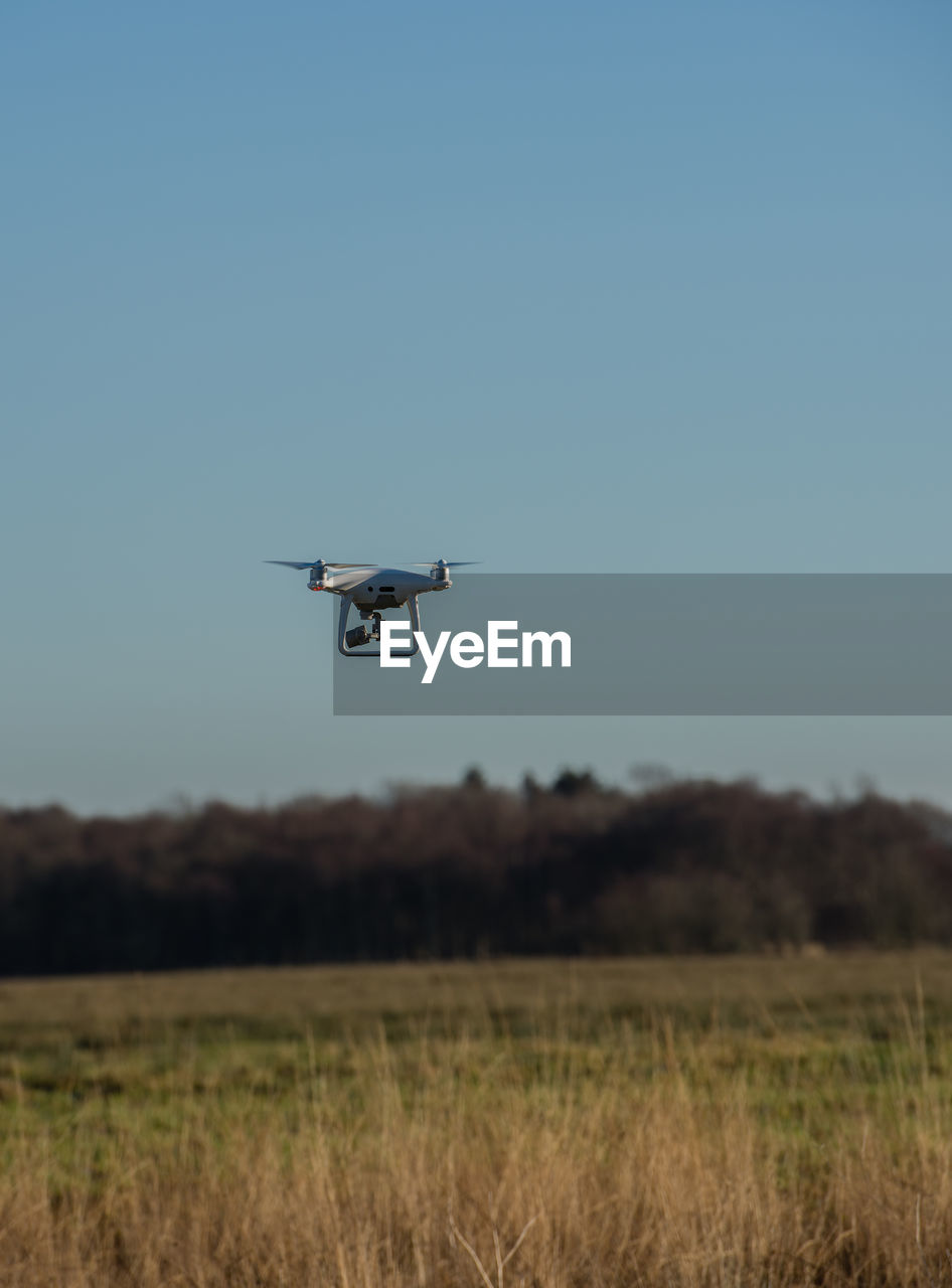 Drone flying over field against clear sky