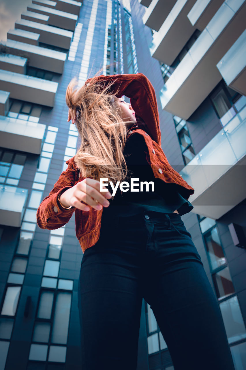 Low angle view of young woman standing against buildings in city