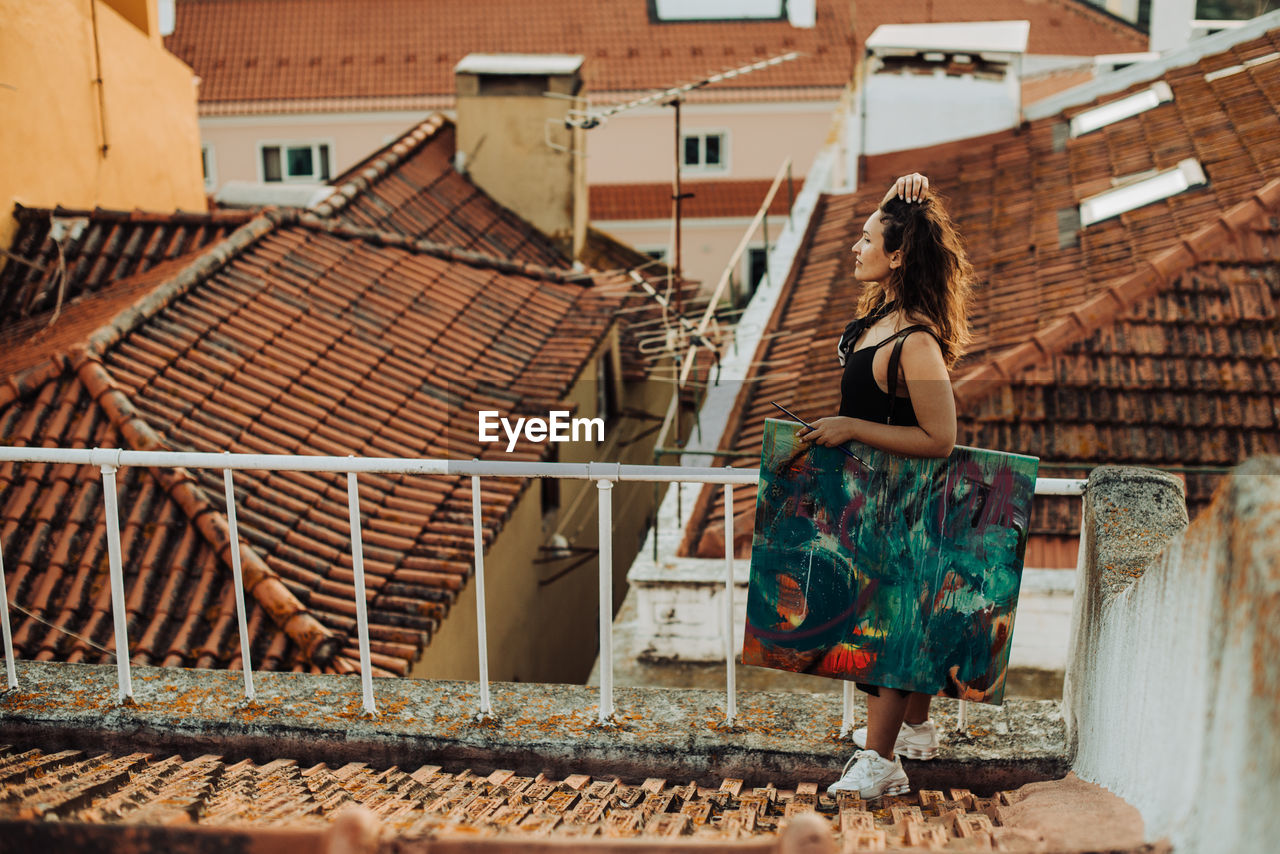 Woman standing holding abstract art painting while standing on roof