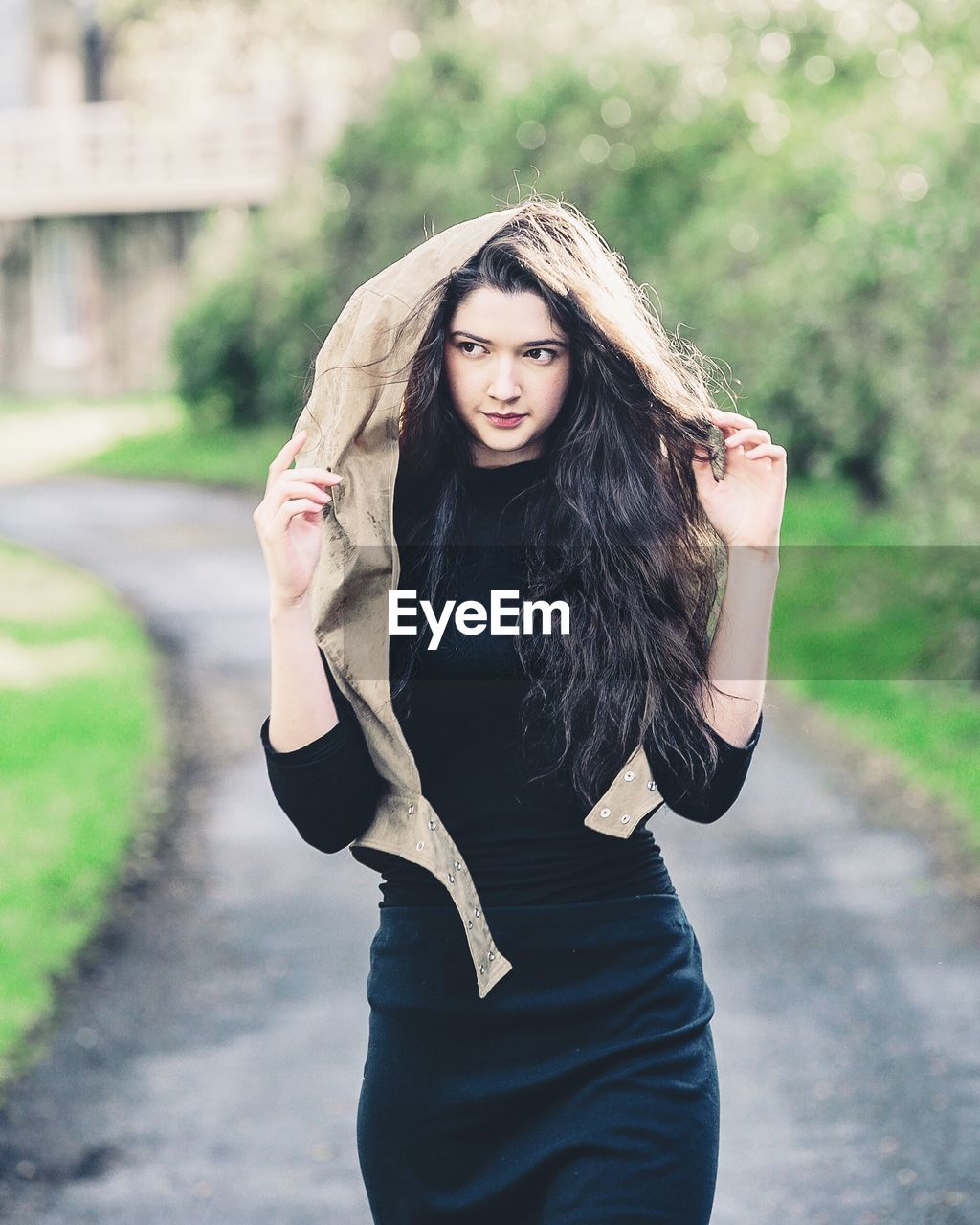 PORTRAIT OF YOUNG WOMAN STANDING AGAINST BLURRED BACKGROUND