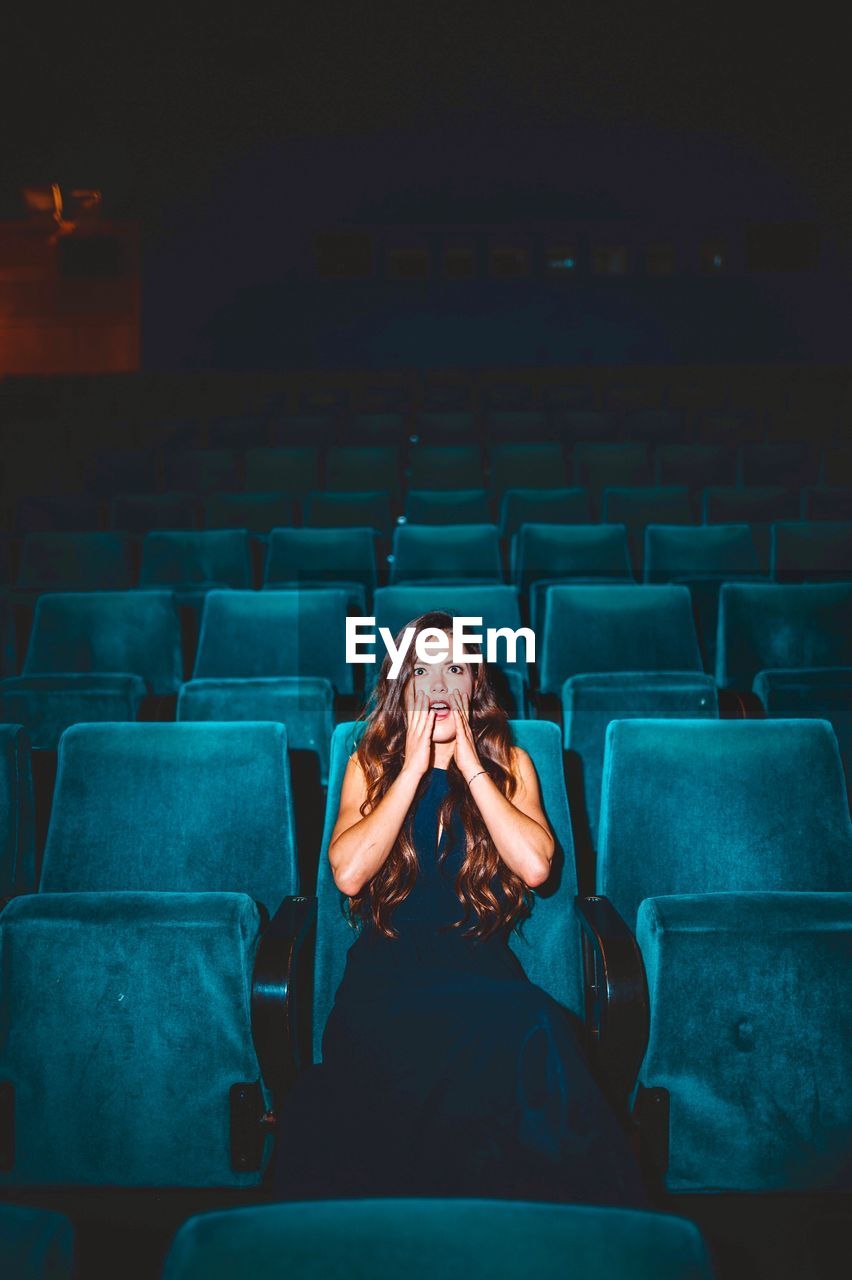 Shocked young woman looking away while sitting on seat in theater