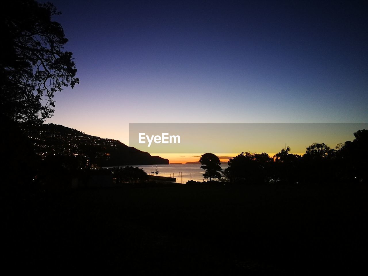 SILHOUETTE TREES BY MOUNTAINS AGAINST CLEAR SKY DURING SUNSET