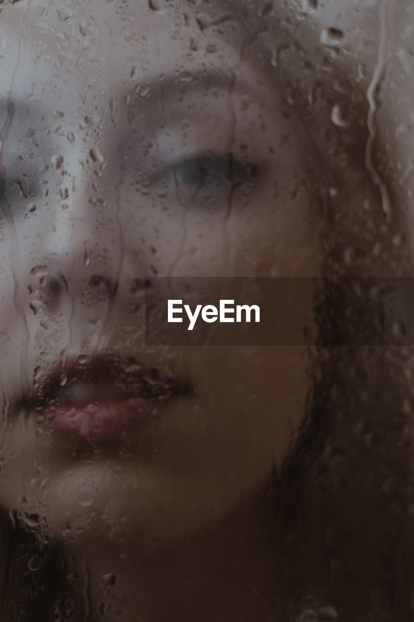 Close-up of woman looking behind wet glass