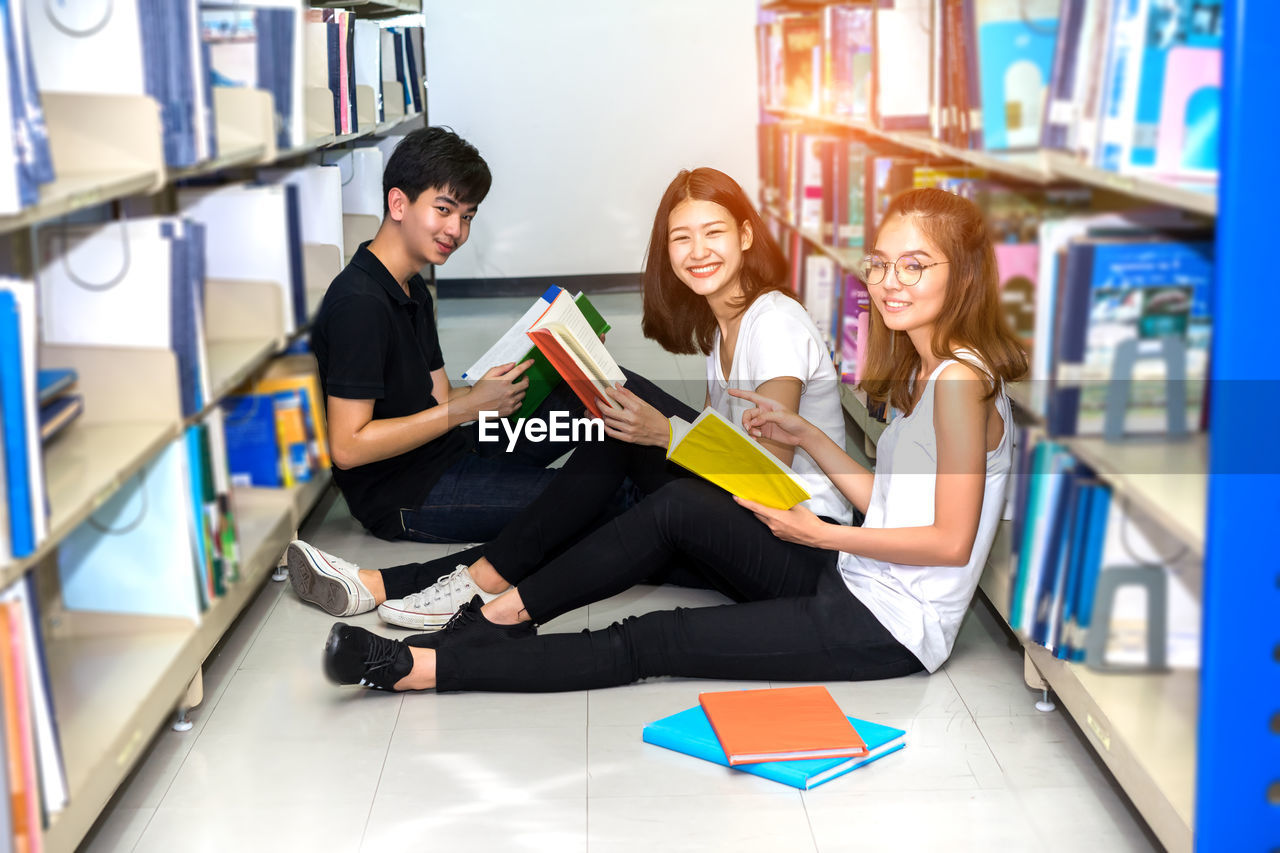 High angle portrait of happy friends studying while sitting on floor in library