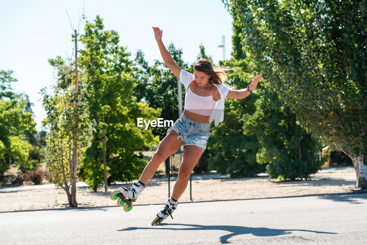 Young fit female in rollerblades showing stunt on road in city in summer