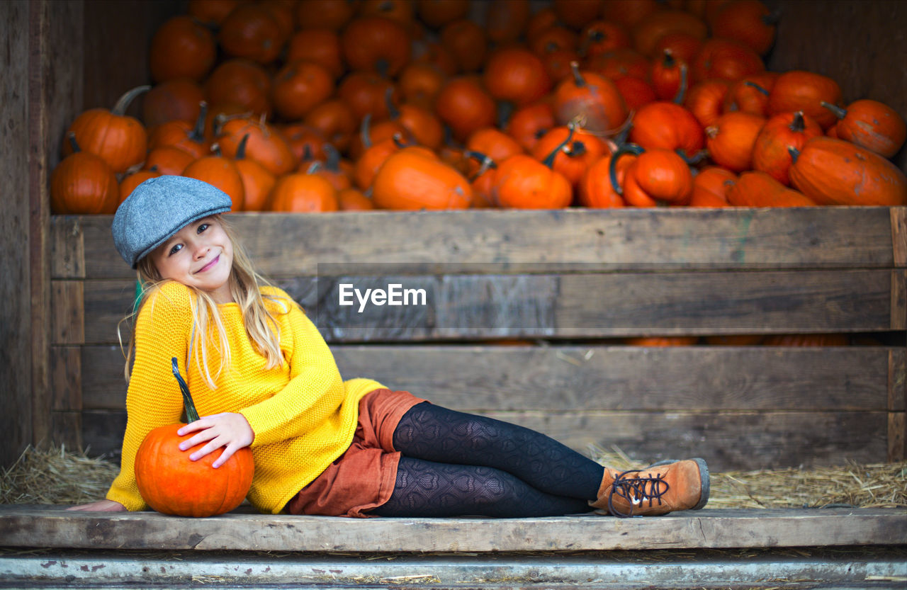 PORTRAIT OF A SMILING YOUNG WOMAN SITTING ON PUMPKIN