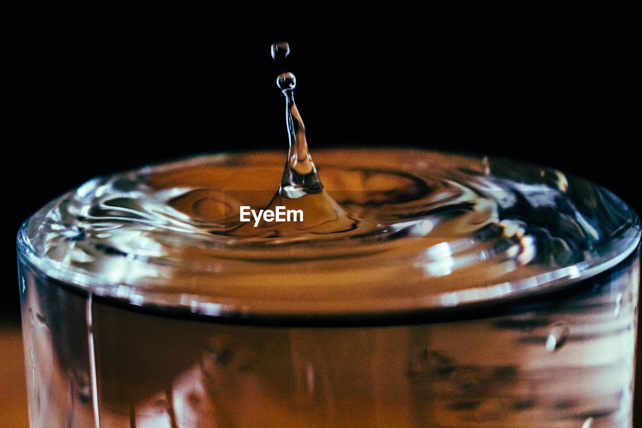 Close-up of water drop splashing in drinking glass against black background